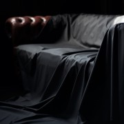 Sheets of San Francisco Black Fluid proof Sex Sheet draped over a dark red leather Cherfield against a dark background