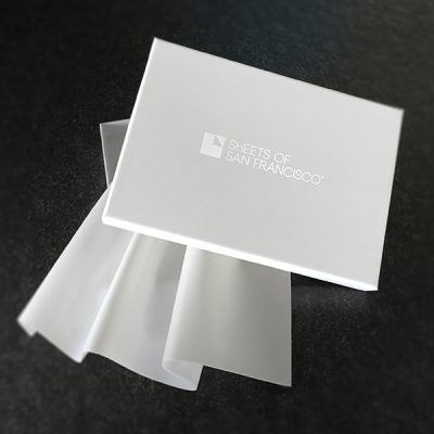 Plus fabric sample and White Box with Sheets of San Francisco logo in white and a white fluidproof fabric sample spilling out