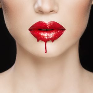 close up of white womans face from nose to neck with dripping gloss red lips to suggest a vampire