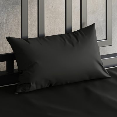 Close up of a Sheets of San Francisco black waterproof pillow case on a bed covered in a Sheets of San Francisco Black fluid proof fitted sheet and against a black metal bedhead with the polished concrete wall behind showing through.