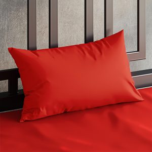 Close up of a Sheets of San Francisco Red waterproof pillow case on a bed covered in a Red Sheets of San Francisco fluid proof fitted sheet and against a black metal bedhead with the polished concrete wall behind showing through.